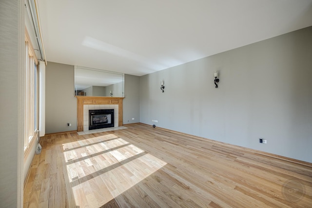 unfurnished living room featuring a tiled fireplace, light wood-style flooring, and baseboards