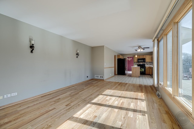 unfurnished living room with visible vents, a healthy amount of sunlight, light wood-type flooring, and a ceiling fan