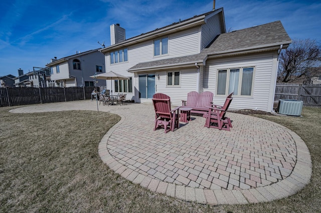 rear view of house with a patio, a fenced backyard, a yard, roof with shingles, and central AC unit