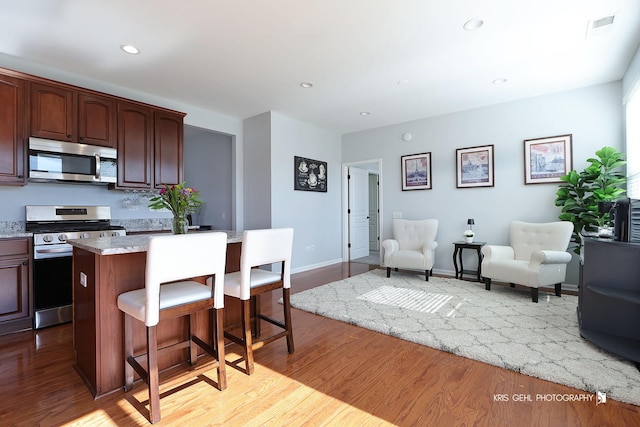 kitchen featuring wood finished floors, visible vents, a kitchen island, a breakfast bar, and stainless steel appliances