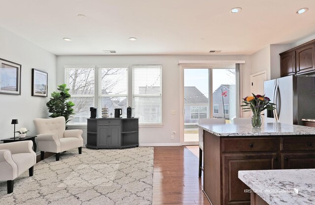 kitchen featuring visible vents, dark brown cabinetry, light stone counters, freestanding refrigerator, and wood finished floors