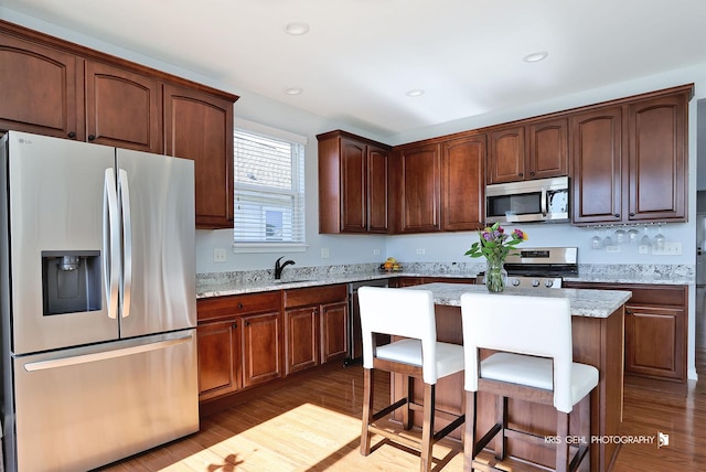 kitchen featuring a kitchen island, a sink, stainless steel appliances, dark wood-type flooring, and a kitchen bar