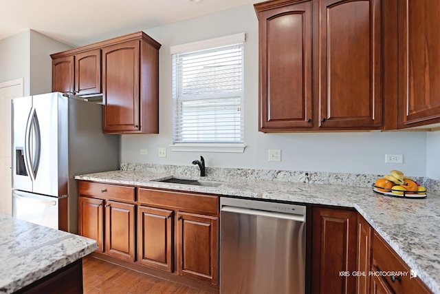 kitchen with light stone countertops, wood finished floors, a sink, appliances with stainless steel finishes, and brown cabinets