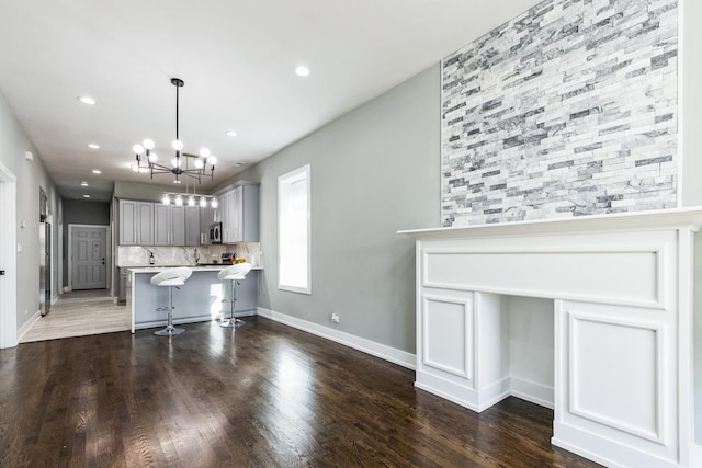 kitchen with gray cabinetry, light countertops, stainless steel microwave, a kitchen breakfast bar, and tasteful backsplash