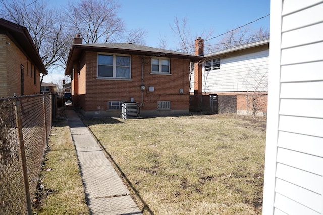 back of house with central air condition unit, fence, a yard, brick siding, and a chimney