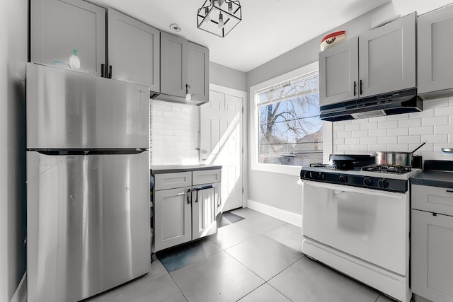 216 W 105th St, Chicago, IL 60628 - kitchen with under cabinet range hood, white gas range, freestanding refrigerator, and gray cabinetry