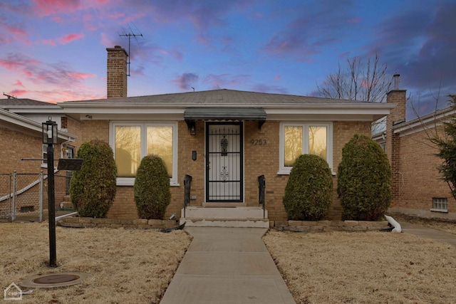 view of front of home featuring brick siding, a chimney, and fence