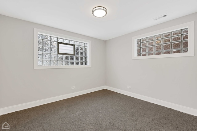 spare room featuring visible vents, baseboards, and dark colored carpet