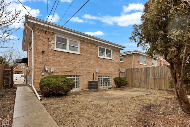 rear view of house with central AC unit, fence, brick siding, and a patio