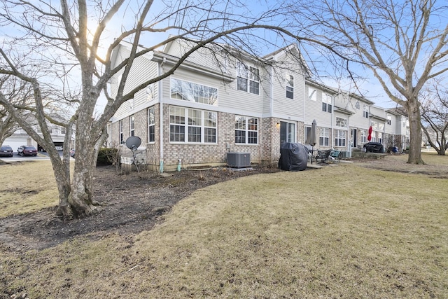 back of house with brick siding, a residential view, a lawn, and central AC unit