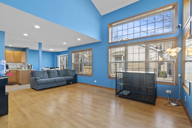 living area featuring recessed lighting, light wood-style floors, baseboards, and a towering ceiling