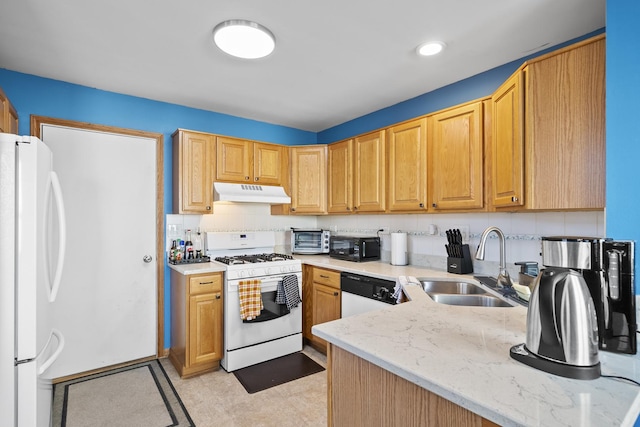 kitchen featuring under cabinet range hood, light stone counters, a sink, backsplash, and white appliances