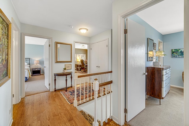 hallway with an upstairs landing, carpet, baseboards, and wood finished floors