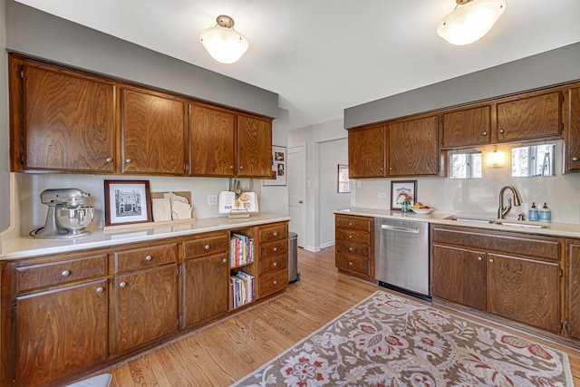 kitchen featuring brown cabinets, light wood-style flooring, a sink, light countertops, and dishwasher