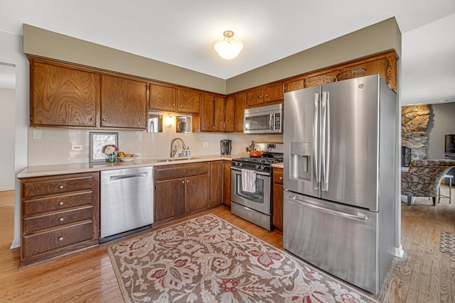 kitchen with brown cabinets, light wood finished floors, a sink, appliances with stainless steel finishes, and light countertops