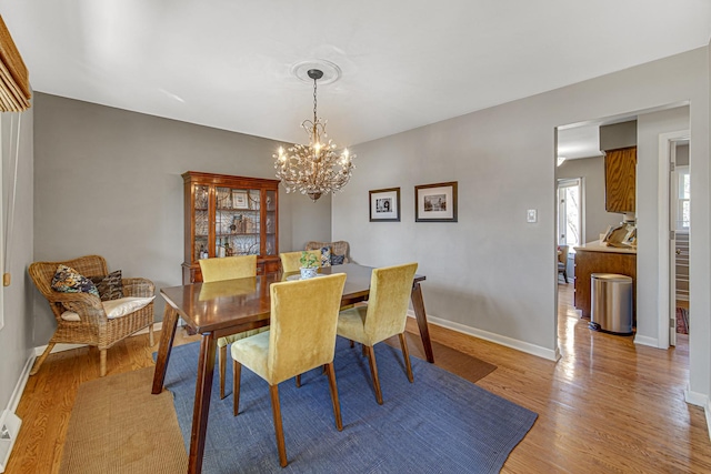 dining room featuring a notable chandelier, baseboards, and light wood-type flooring