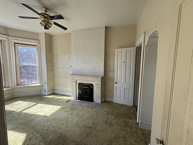 unfurnished living room with baseboards, a fireplace with flush hearth, a ceiling fan, and carpet