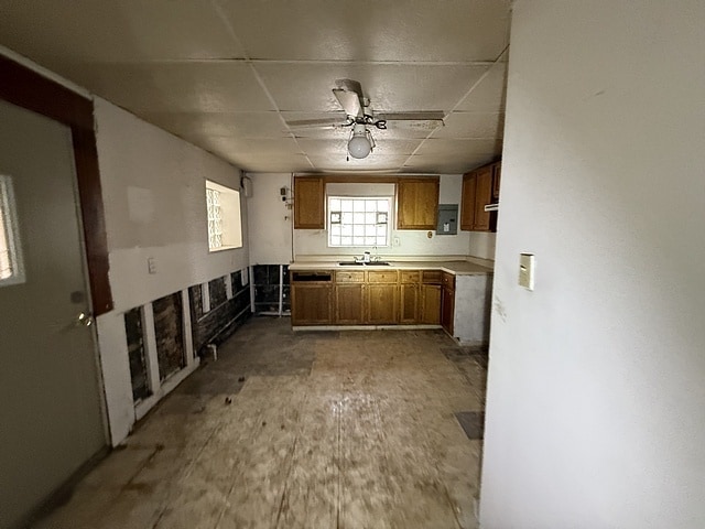 kitchen with light countertops, brown cabinets, a paneled ceiling, a ceiling fan, and a sink