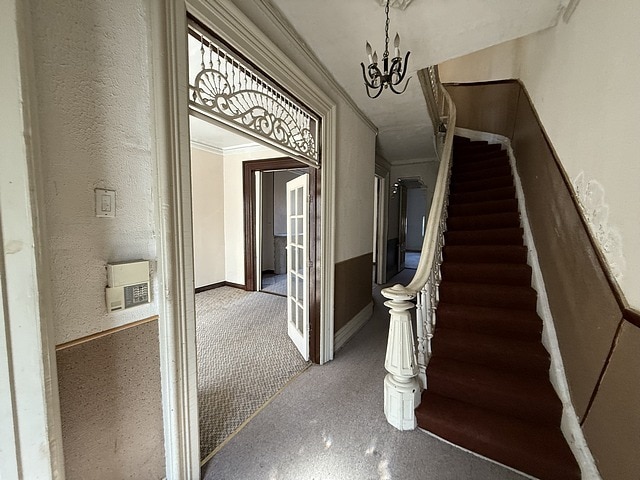 staircase with crown molding, a notable chandelier, a textured wall, and baseboards