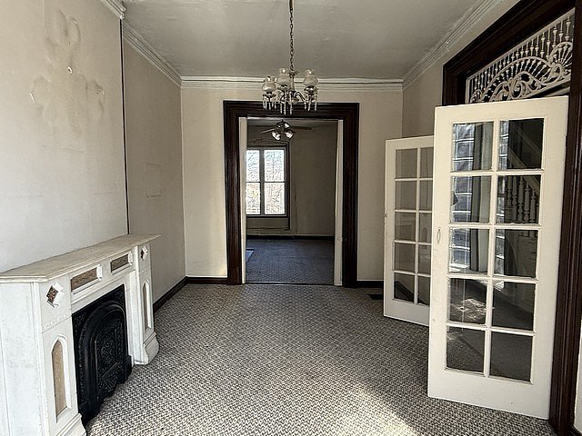 unfurnished dining area with carpet floors, french doors, a fireplace, and ornamental molding