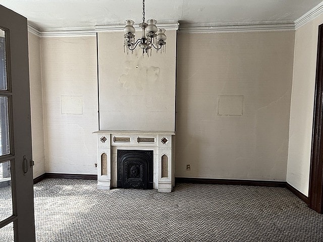 unfurnished living room with carpet, baseboards, a fireplace, crown molding, and a chandelier