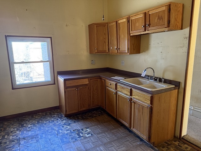 kitchen with a sink, baseboards, dark countertops, and brown cabinetry