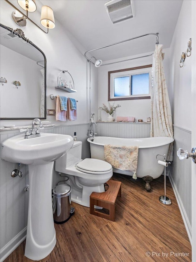 bathroom featuring visible vents, a freestanding bath, toilet, wainscoting, and wood finished floors