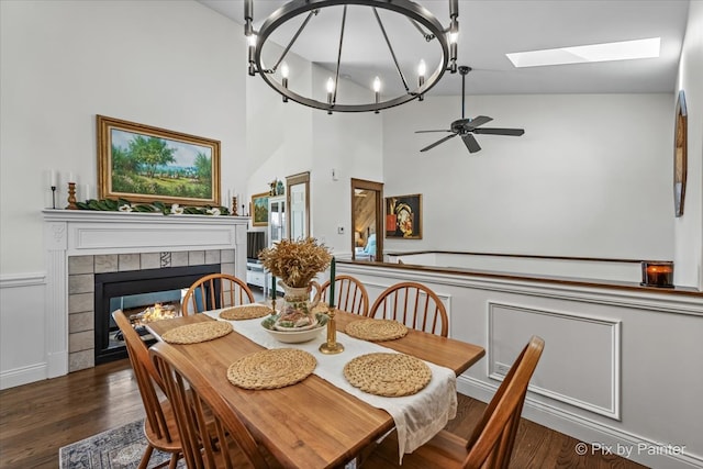 dining area with a skylight, a ceiling fan, wood finished floors, and a tiled fireplace