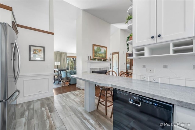 kitchen featuring a tiled fireplace, open shelves, black dishwasher, freestanding refrigerator, and white cabinets