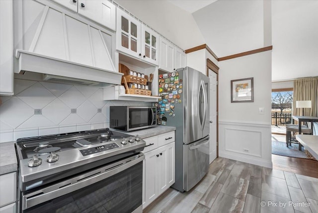 kitchen featuring custom range hood, white cabinets, appliances with stainless steel finishes, and wainscoting