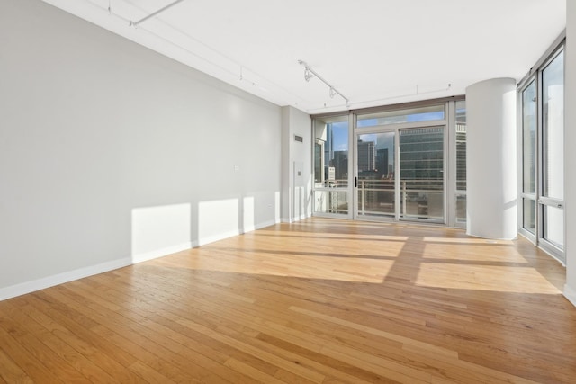 spare room with a view of city, track lighting, hardwood / wood-style floors, a wall of windows, and baseboards