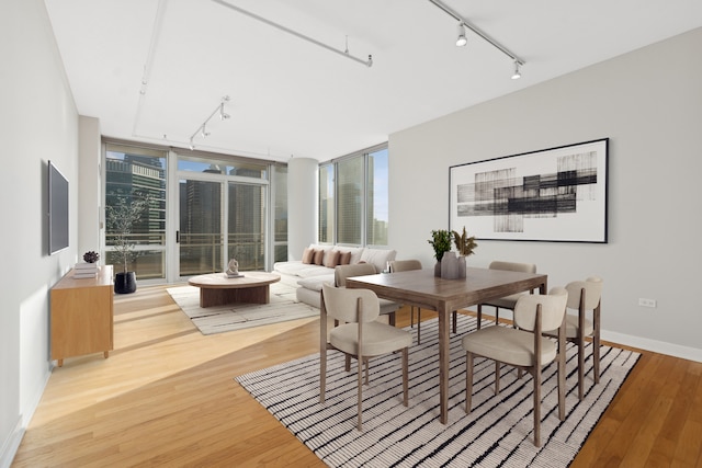 dining room featuring a city view, track lighting, light wood-style floors, and baseboards