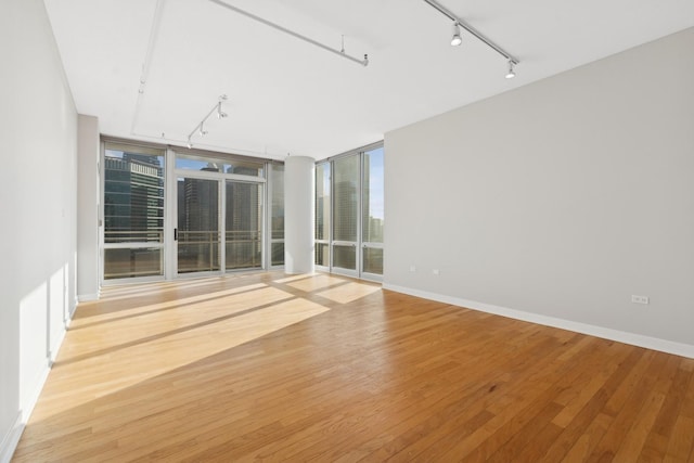 empty room featuring rail lighting, baseboards, light wood-style floors, and expansive windows