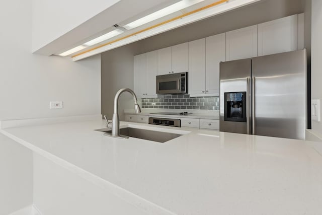 kitchen featuring a peninsula, a sink, decorative backsplash, appliances with stainless steel finishes, and white cabinetry