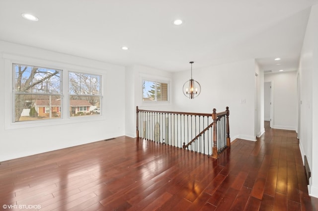 corridor featuring an upstairs landing, a notable chandelier, a wealth of natural light, and dark wood-style flooring