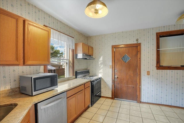 kitchen featuring under cabinet range hood, stainless steel appliances, wallpapered walls, light tile patterned floors, and baseboards