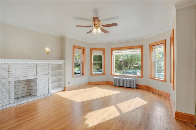 unfurnished living room featuring a brick fireplace, radiator, built in shelves, ornamental molding, and wood finished floors