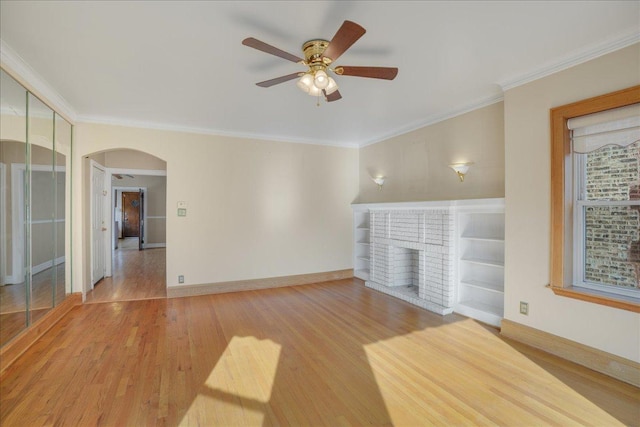 spare room featuring light wood-style floors, crown molding, a fireplace, and arched walkways