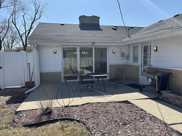 rear view of house featuring a gate, fence, roof with shingles, brick siding, and a patio area