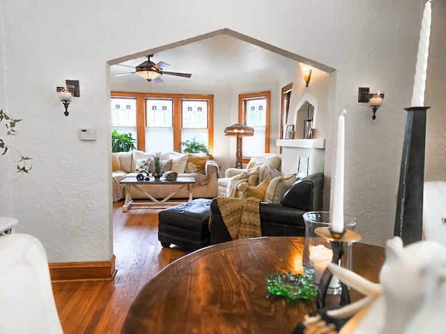 living room featuring a textured wall, baseboards, ceiling fan, and hardwood / wood-style flooring