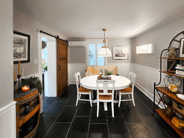 dining space featuring dark tile patterned floors, a barn door, a wainscoted wall, and a wall unit AC