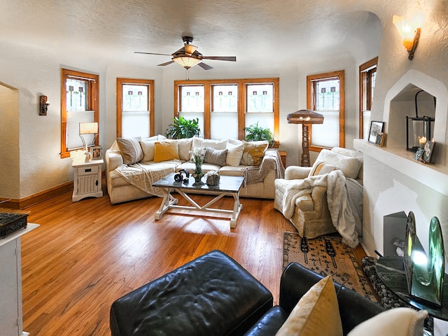 living room with a ceiling fan, wood finished floors, baseboards, a textured ceiling, and a textured wall