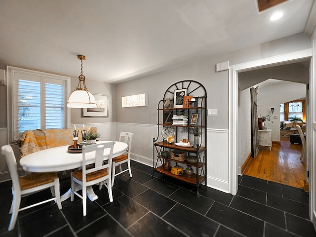 dining area featuring dark tile patterned flooring, arched walkways, and a wainscoted wall