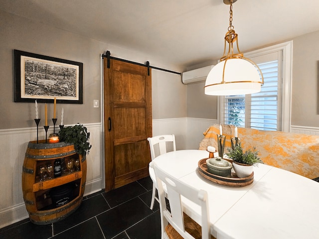 dining space featuring a wainscoted wall, a barn door, dark tile patterned flooring, and a wall unit AC