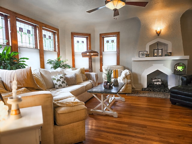 living area with wood finished floors, a ceiling fan, a textured wall, and a large fireplace