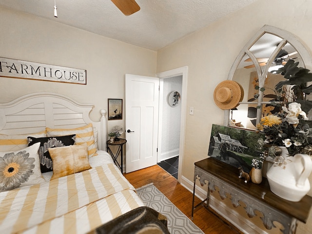 bedroom with a textured ceiling, a ceiling fan, baseboards, and wood finished floors