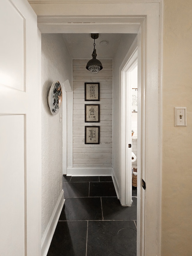 hall featuring a textured wall, baseboards, and wood walls