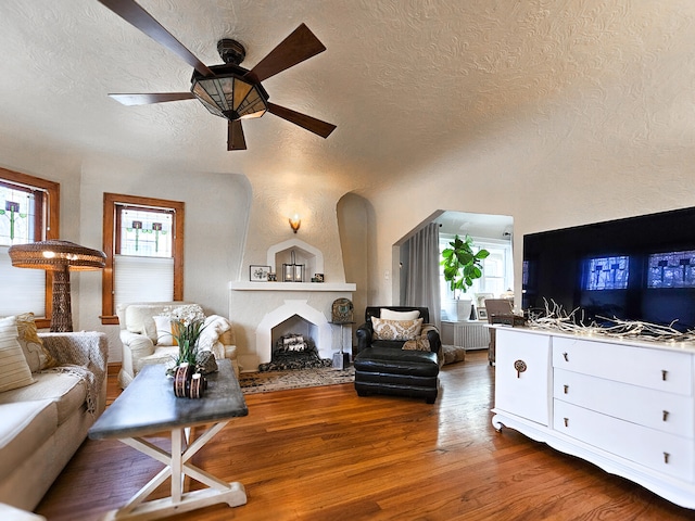 living room with radiator heating unit, a fireplace, wood finished floors, a textured ceiling, and a ceiling fan