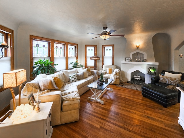 living room featuring dark wood-type flooring, a large fireplace, arched walkways, and ceiling fan