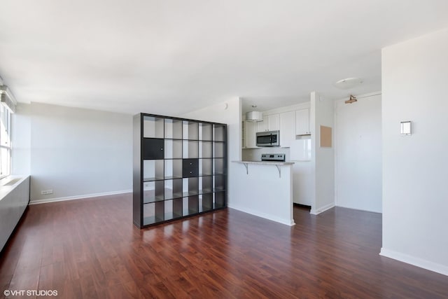 unfurnished living room with dark wood-type flooring and baseboards